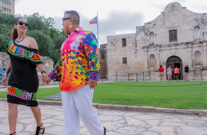Two people in bright clothing holding hands in front of the Alamo